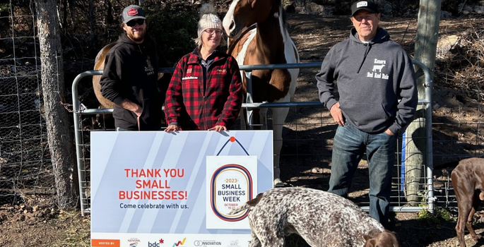 three people standing with a Small Business Week sign in front of a farm gate, a horse is behind the gate.
